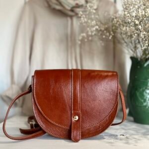 Ce sac porté croisé en cuir de vachette allie élégance et praticité. Son rabat aimanté assure une fermeture sécurisée, tandis que sa bandoulière réglable offre un confort optimal. Grâce à sa forme arrondie, l’espace intérieur est optimisé pour ranger facilement tous vos essentiels.